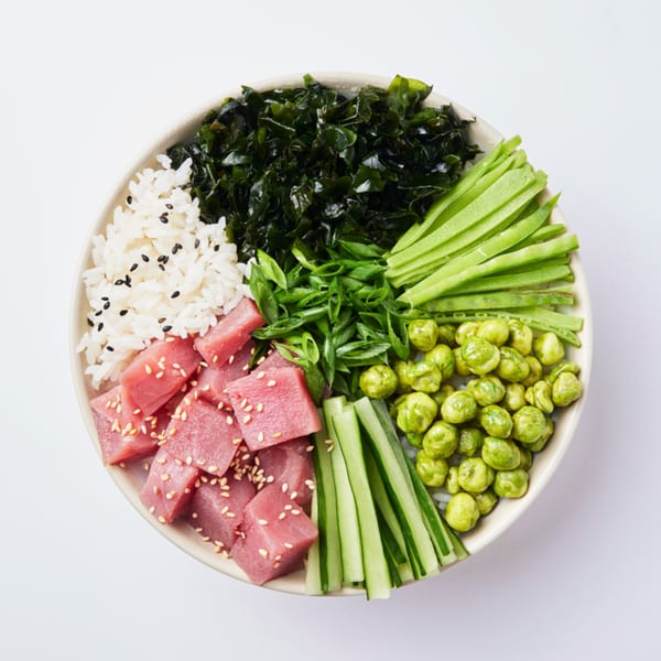 Overhead view of a colorful Inti Poke bowl with tuna, rice, seaweed, cucumber, scallions, and wasabi peas.